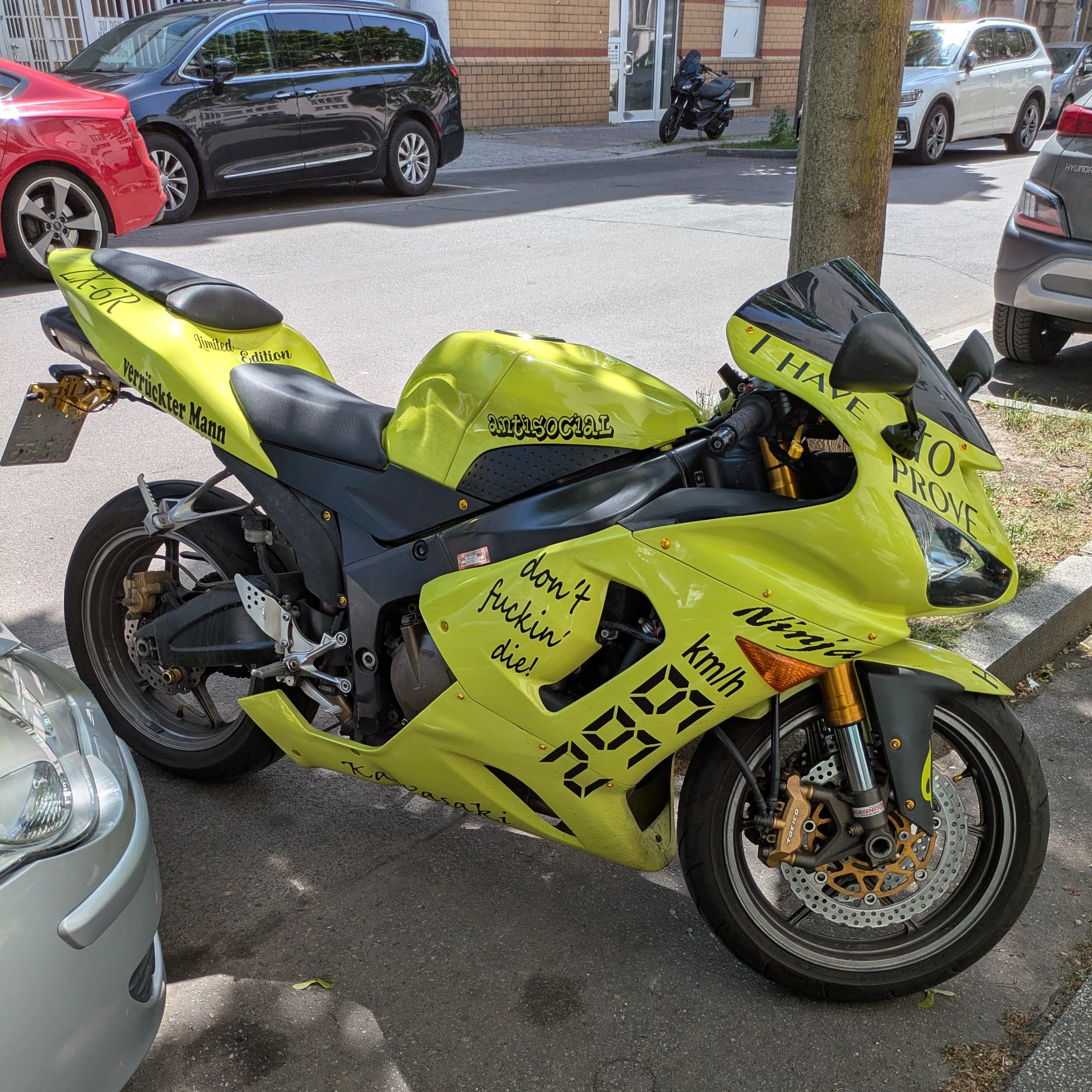 ein parkendes motorrad im straßenraum, andere parkende autos sind sichtbar. das motorrad ist knallgelb lackiert und mit diversen sprüchen ergänzt

- dont fuckin die
- 299 km/h
- I have to prove
- antisocial
- verrückter Mann
